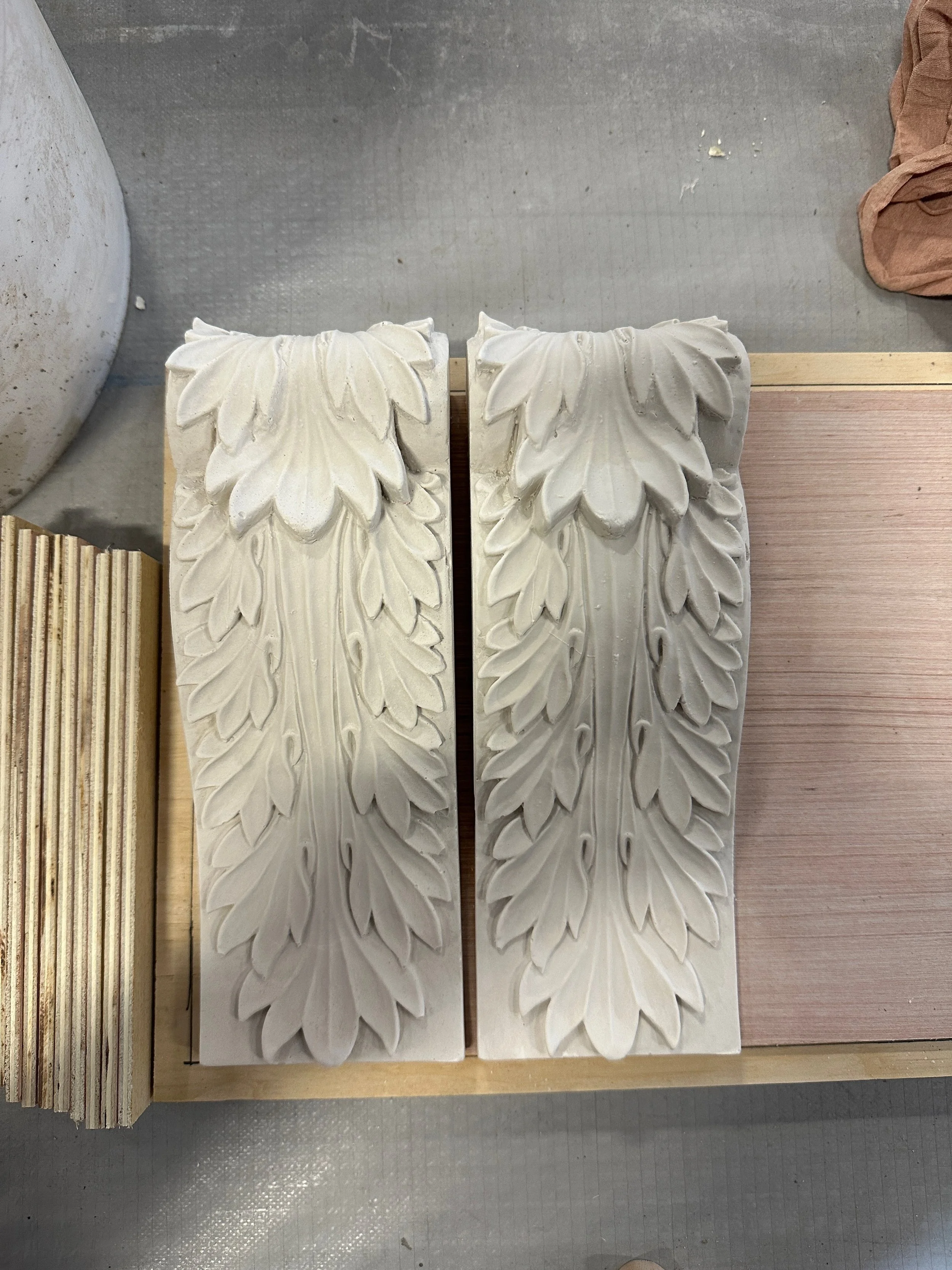 Decorative carved plaster or stone blocks with leaf motifs, placed on a wooden surface.