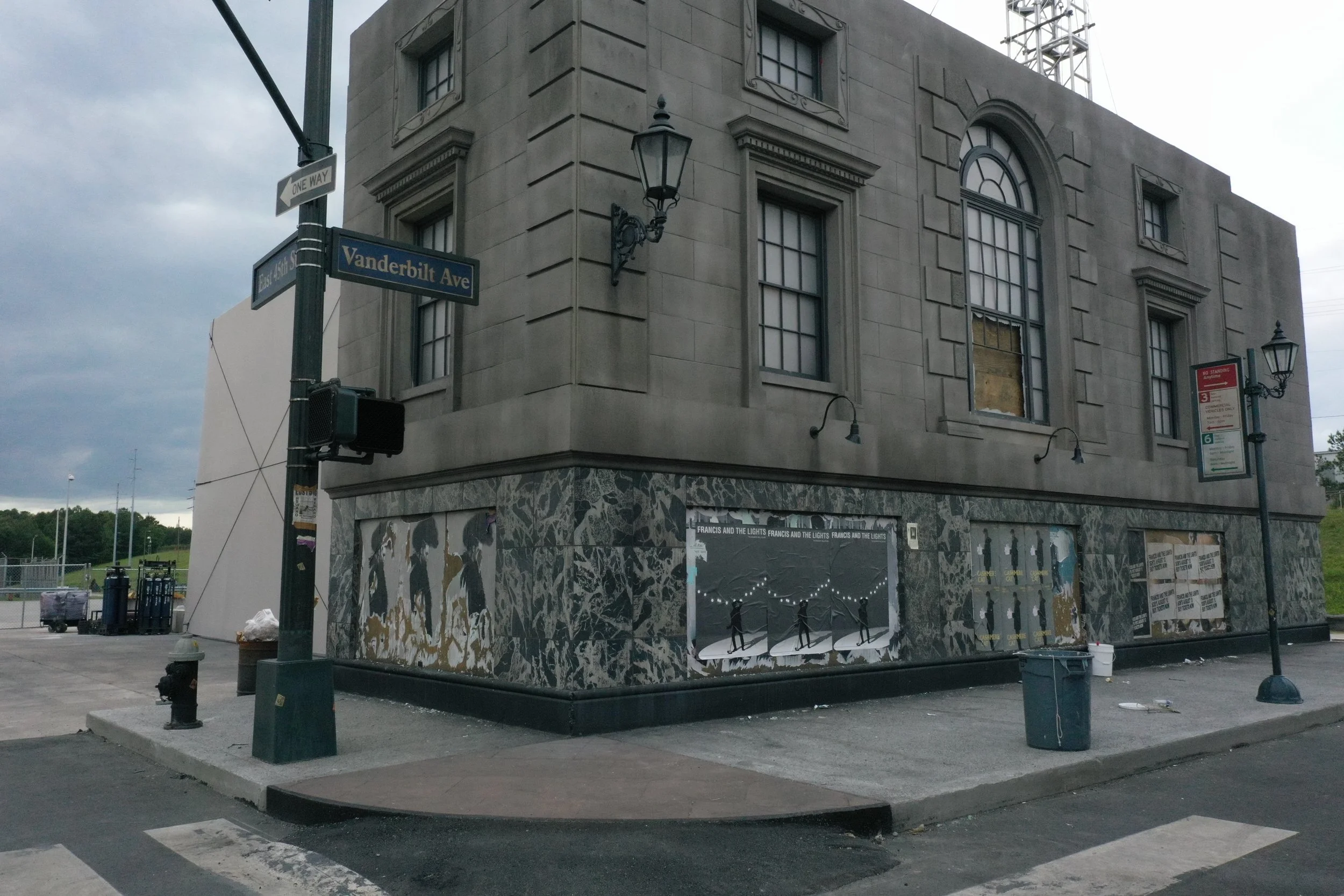 Corner of a building at the intersection of Vanderbilt Avenue and East 65th Street, with street signs, traffic signal, and streetlights, featuring a mural on the ground floor and building architectural details.