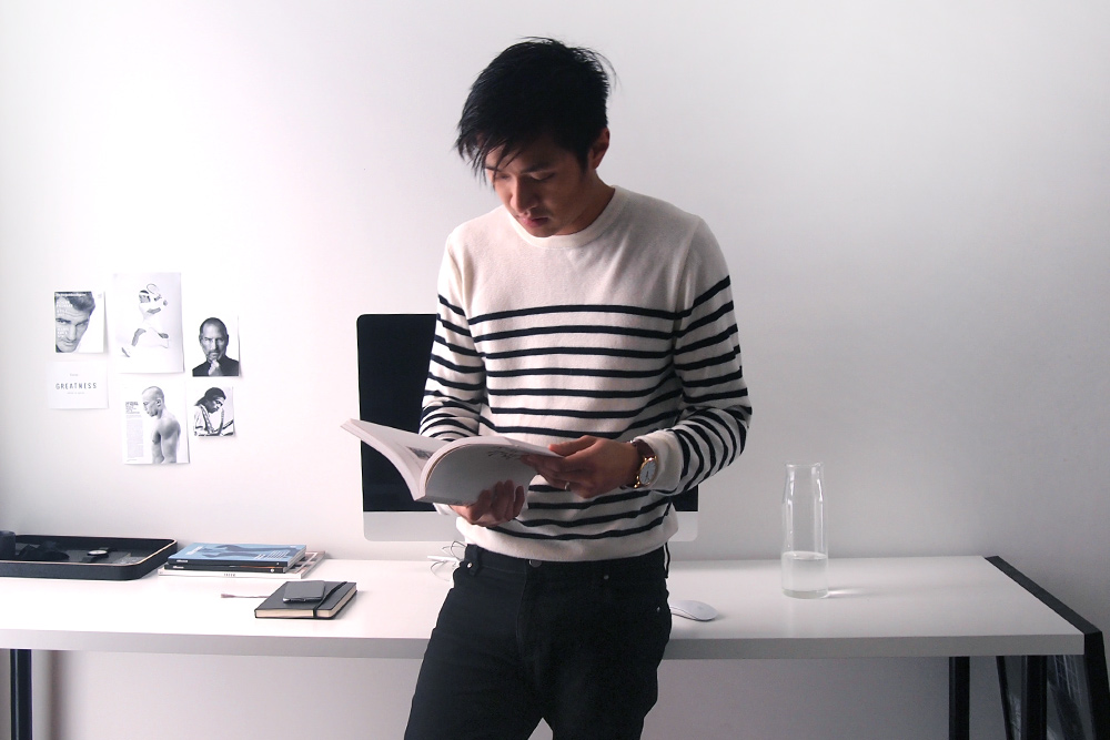 Creative Director Nguyen Le Standing By His Desk and Thumbing Through a Magazine