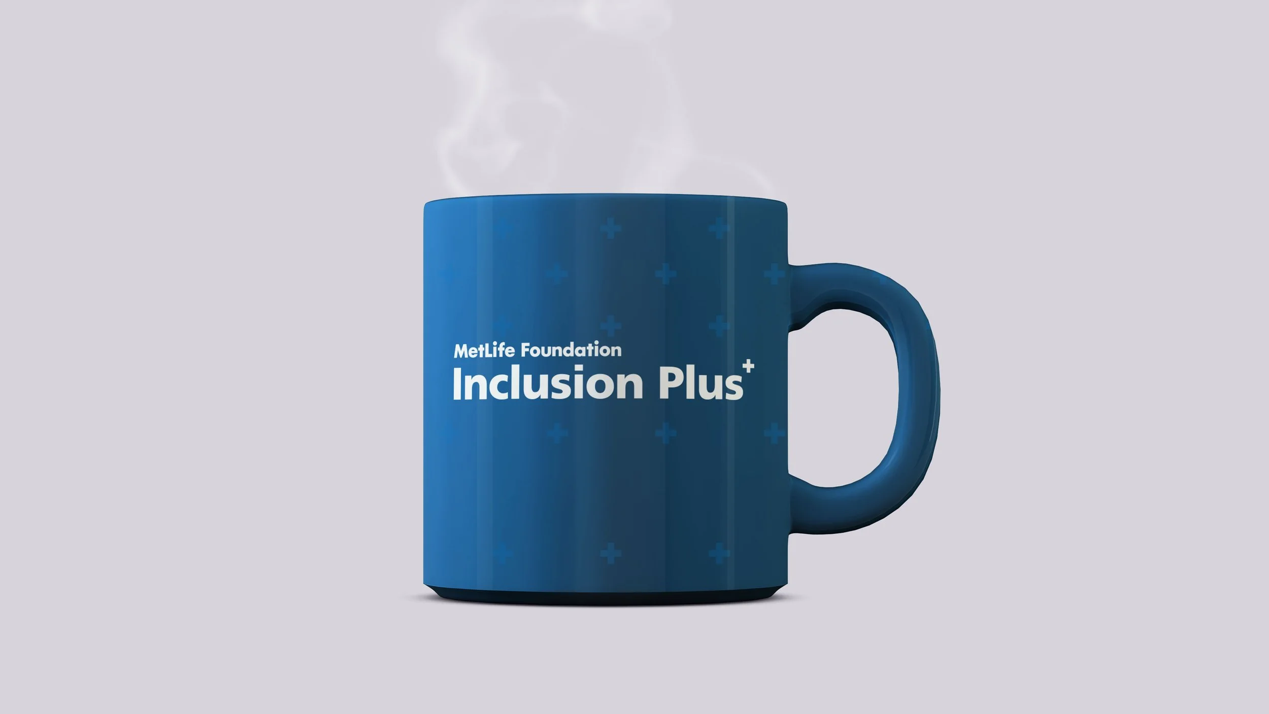 A blue mug with steam rising from it, displaying the text 'MetLife Foundation Inclusion Plus' and small plus signs pattern.