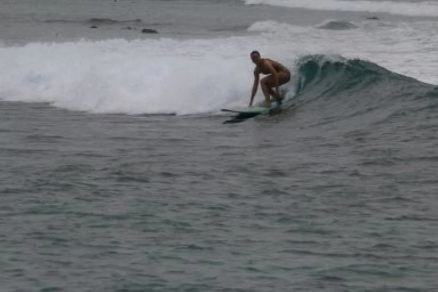 A person surfing on a small wave in the ocean during daylight.