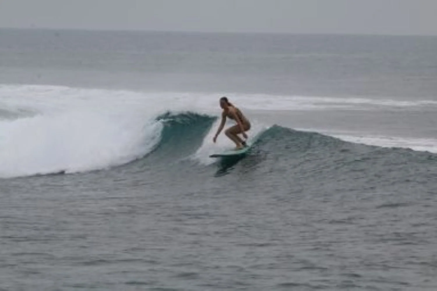 A person surfing on a wave in the ocean under a cloudy sky.