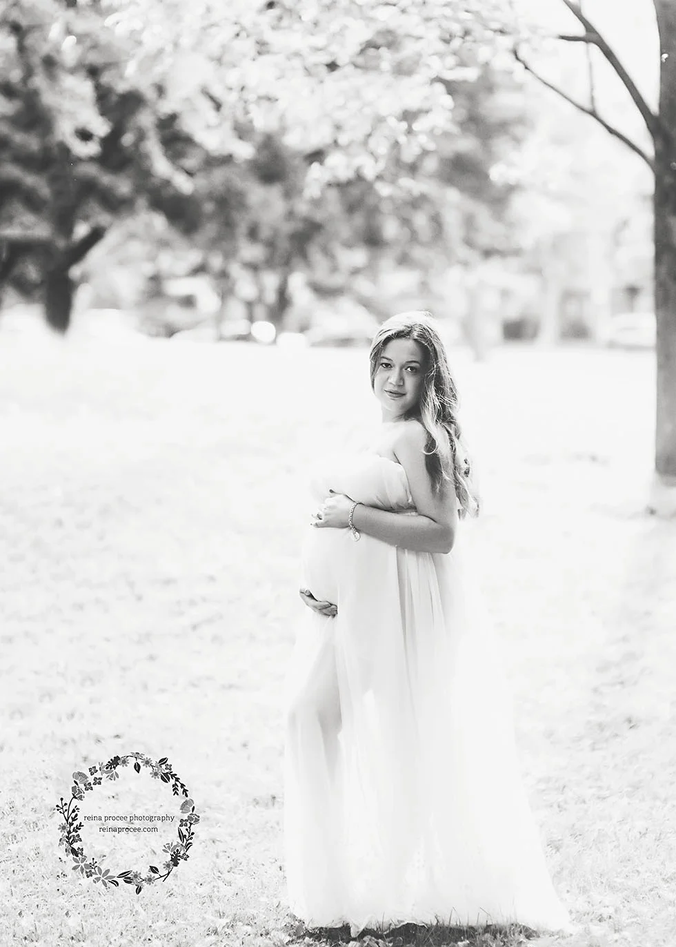 pregnant woman hugging her belly in a field with a cream dress blowing in the wind in black and white