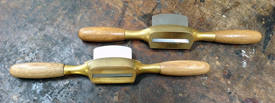 Two Boggs spokeshaves. On the left is a curved bottom for working concave surfaces. On the right is a flat bottom for working flat and convex surfaces.