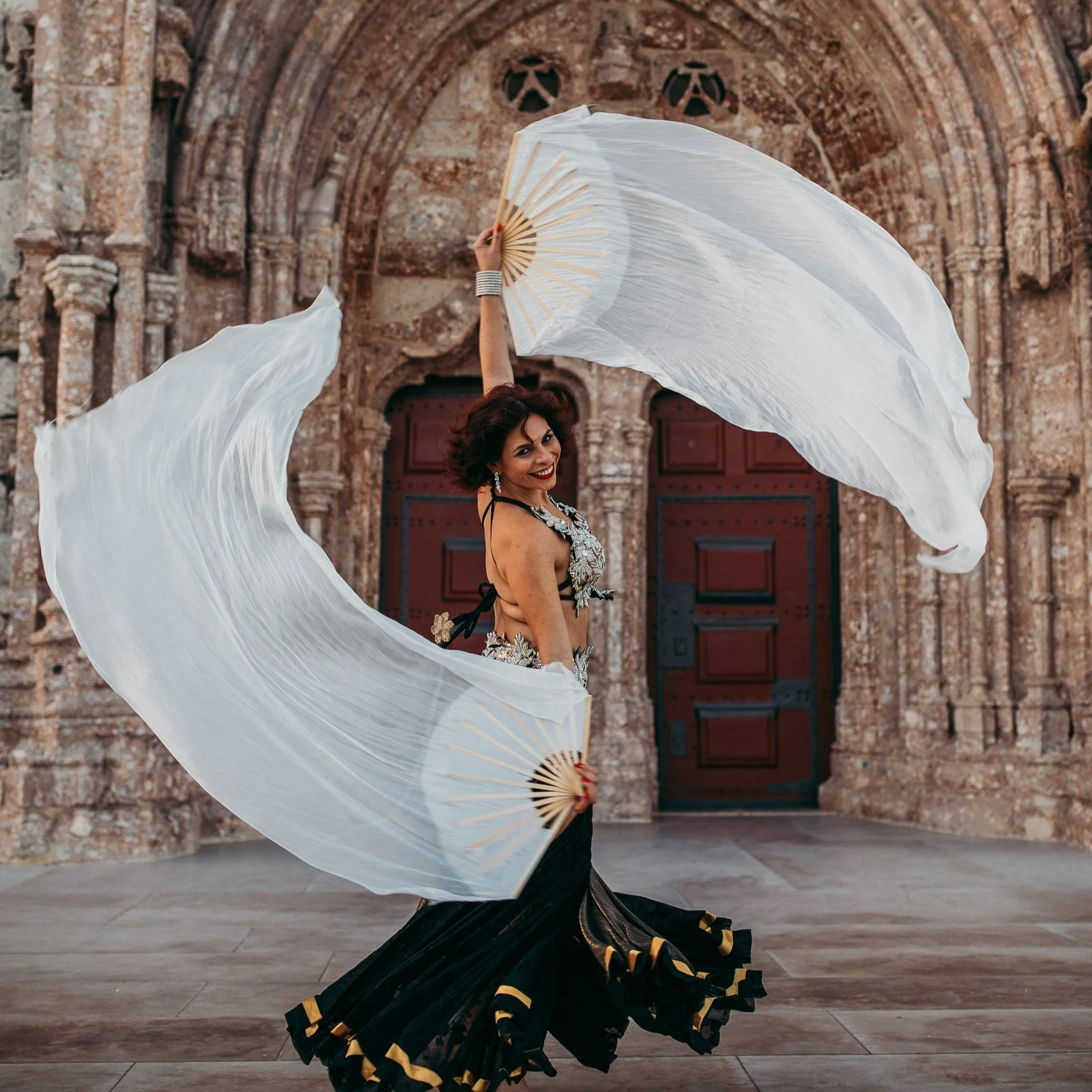 Mulher vestida com traje de dança usando dois lenços brancos em uma escadaria antiga.