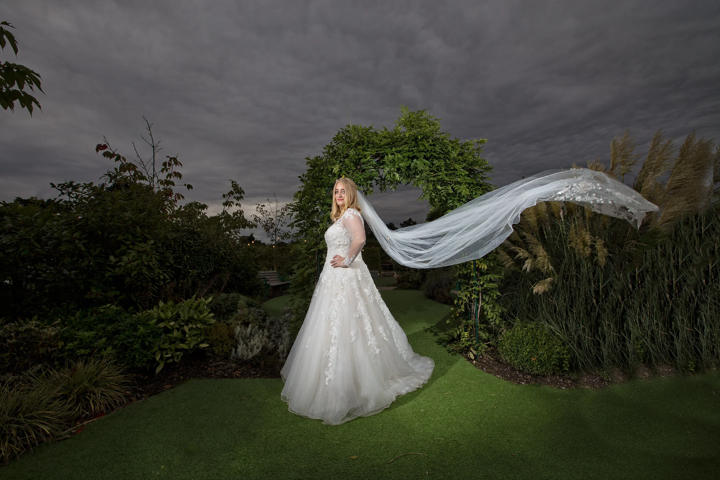 Happy bride on her wedding day with a veil blowing in the evening light.