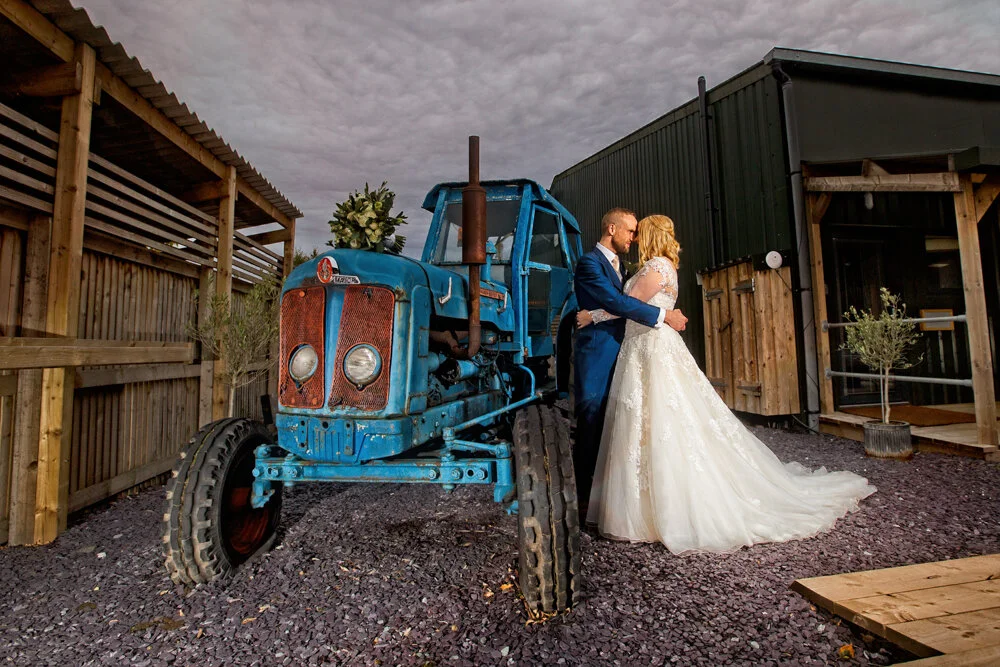 Cheshire Barn wedding /Bride and groom pose with rustic tractor  for photo by Avanti