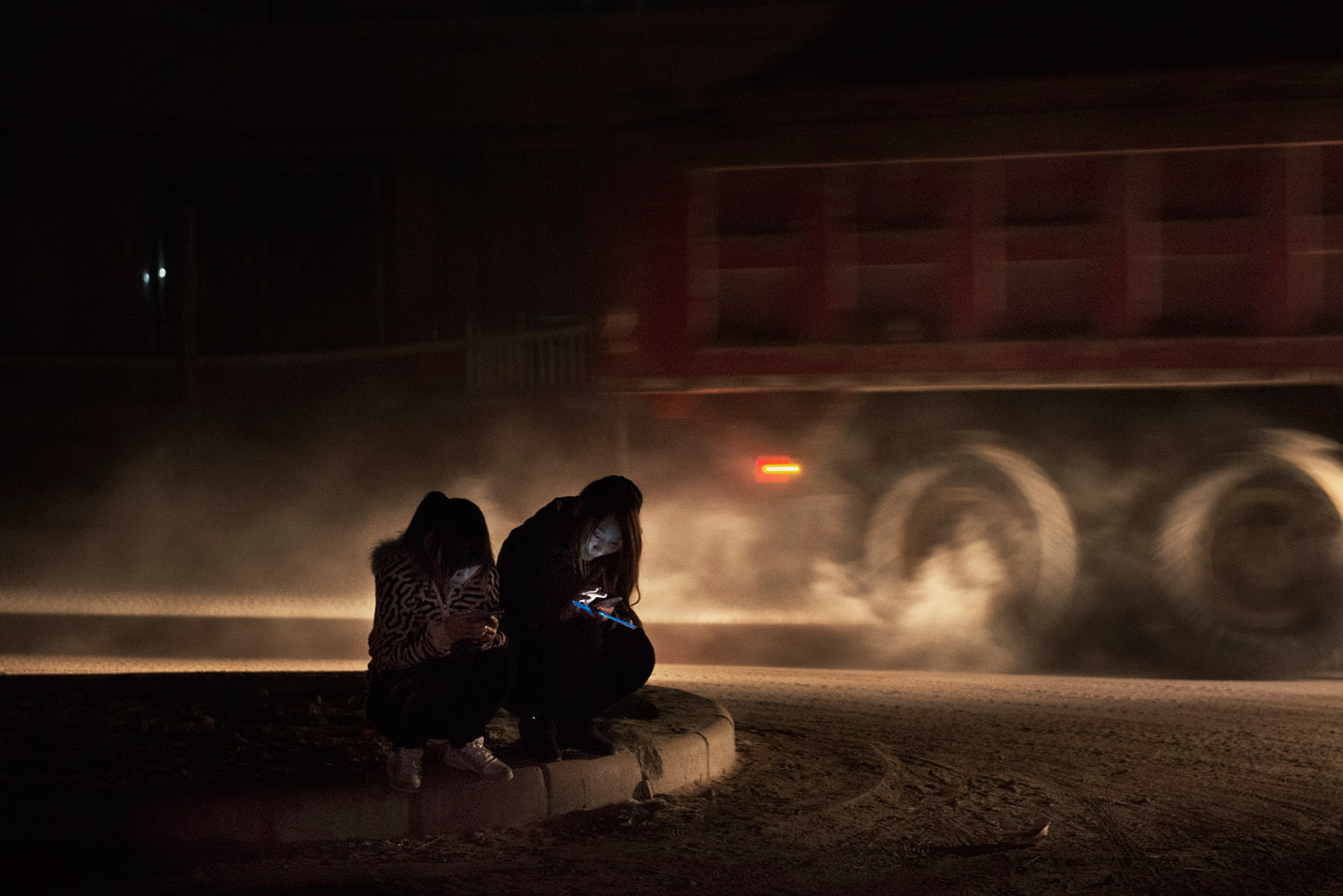 On a dirt road of Foxconn factory town on the outskirts of Zhengzhou, two girls checking their smartphones while a construction truck is passing nearby.