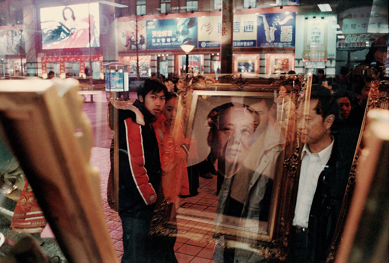 Portraits of Mao refelcts in the window of a photographer store in a commercial artery of Beijing.