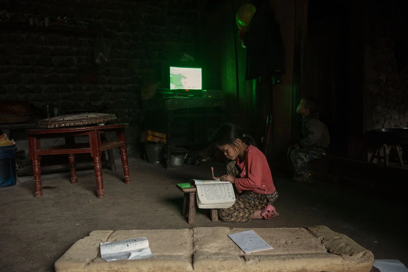 8 years old Ting Fe doing her schoolwork, while her little brother is watching tv. 