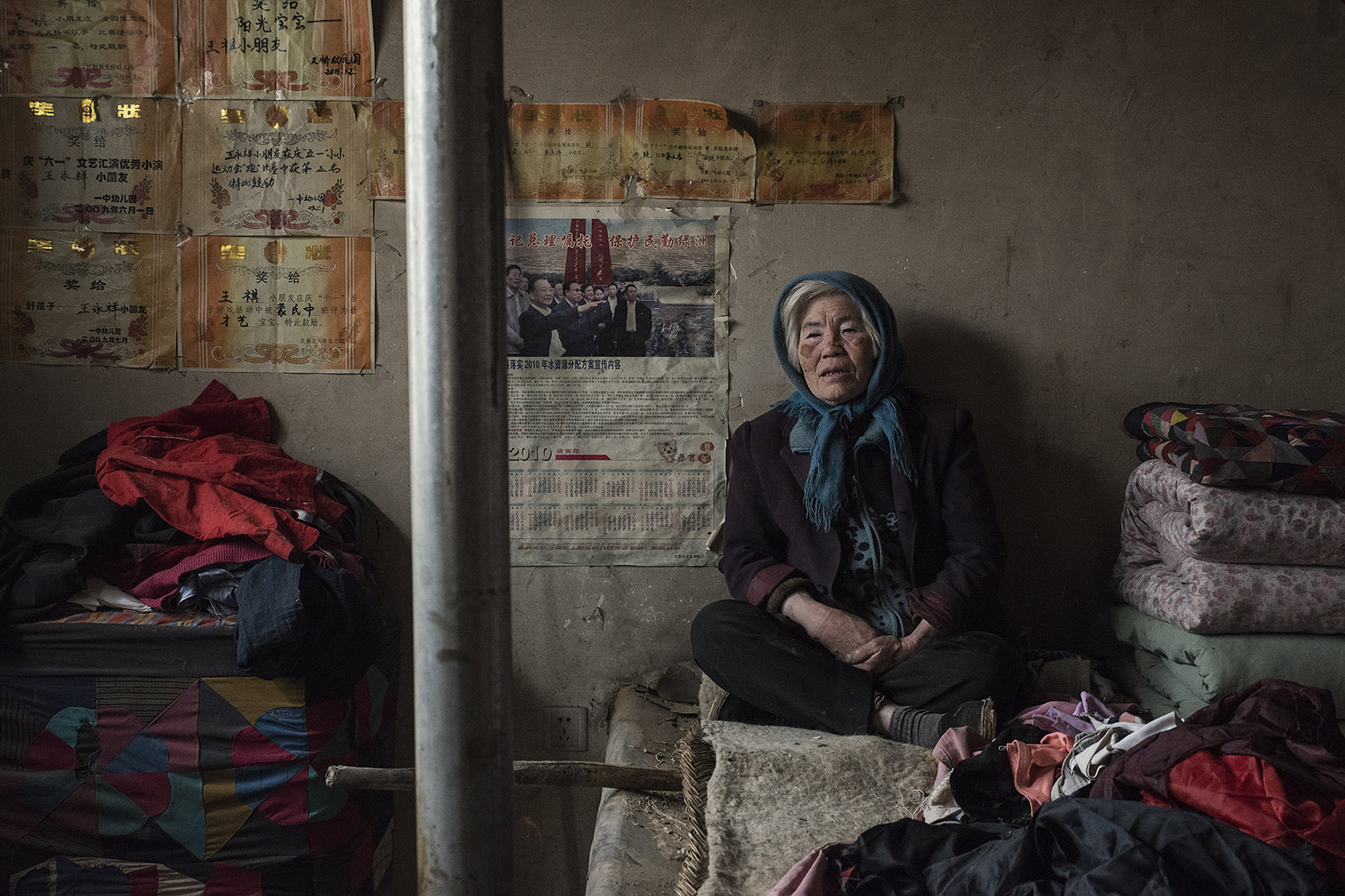 Huanghui new village 65 years old Zheng Julian on her broken kang. 8 years ago Zheng and her family had to leave their village 50 kilometers away officially because of desertification. She complains that the land they were given is no better than the one they left and says the houses built by the government for the relocated farmers are poorly built. "When I had to leave, I cried so much I thought I would become blind." On her wall, the school diplomas and awards of her grandson as well as a 4 years old calendar featuring a picture of Prime Minister Wen Jiabao visiting her region, during which he made a pledge to fight desertification.