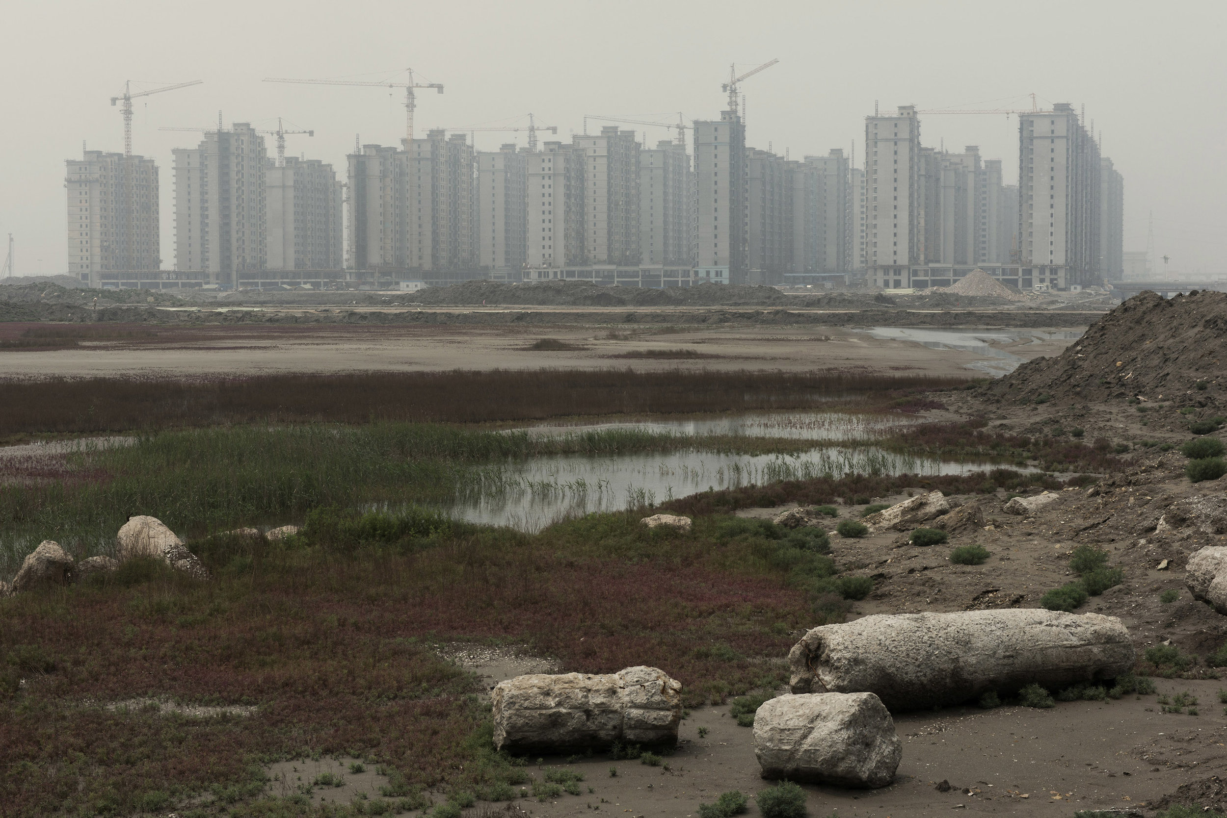 Residential buildings under construction in Caofeidian a new city built on reclaimed land at a high cost. Billed as the "world's first realised eco-city" at its inception, 8 years and billions of dollars later, few industries have moved there and the city is mostly empty. Bad planning, mismanagement, speculation and corruption have led to the creation of many "ghost cities". 