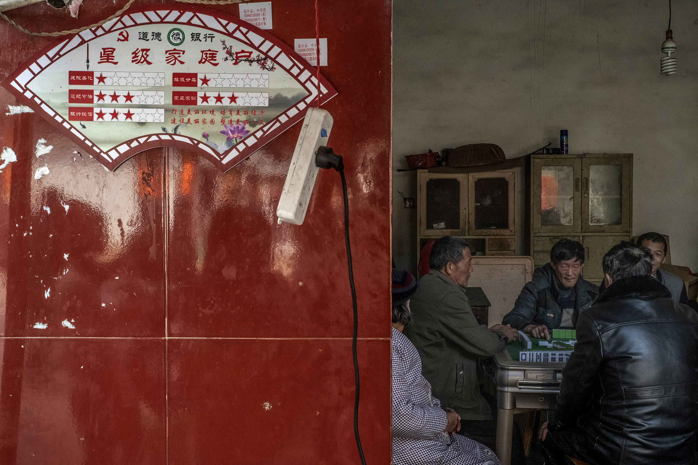 In Yangqiao (Zhejiang) locals are playing Mah-Jong in a home where the household social credit score is displayed on the wall. The social credit system implemented in this village since 2018 is based on five criteria : cleanness and tidiness of courtyard, Observance of laws and regulations, bank credit, recycling, family values. Locals describe the system as useless and of no effect on their daily behaviour (which includes for many, gambling). However, this local experience has been hailed as a success by local and national State media and will be extended to other villages and towns in the region. Chinese authorities have announced their wish to have a nationwide social credit system in place by 2020. However the details and feasibility of such a system are yet unclear.