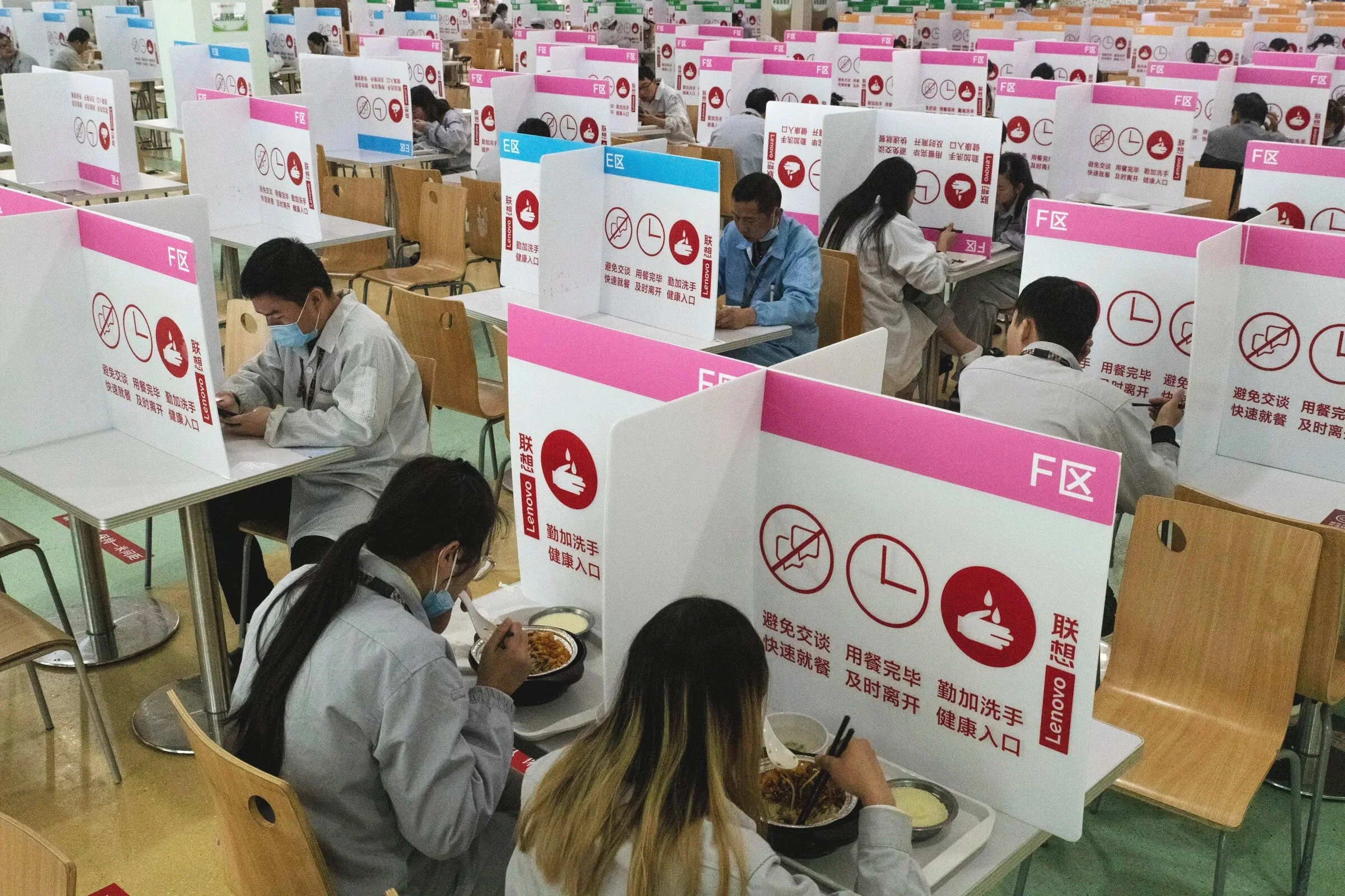  A the canteen of a Lenovo factory producing smartphones and tablets, the formerly communal cafeteria tables have been partitioned off by vertical barriers covered in reminders to avoid conversations. The barriers have been set-up to avoid possible c