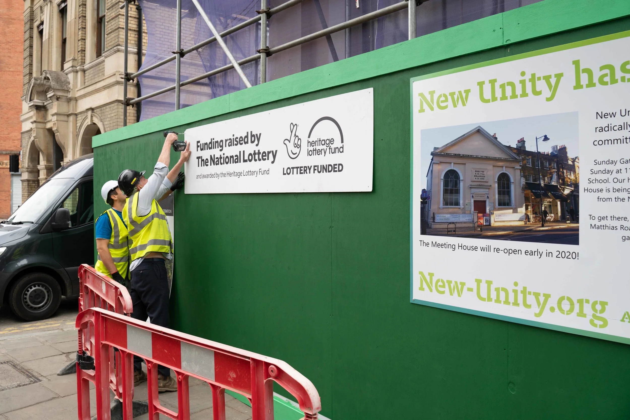 The building team mounting signage on the recently erected green hoarding facing Newington Green