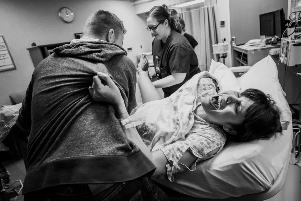 "The Pain She'll Soon Forget" - Laura Eckert I love how this photo fills the frame, first I see her face, then her hand gripping dad, then I'm drawn up to the nurse and the clock. I love the wide angle - and how flattering this image is of mom even in such an intense moment. She looks beatufiul! 