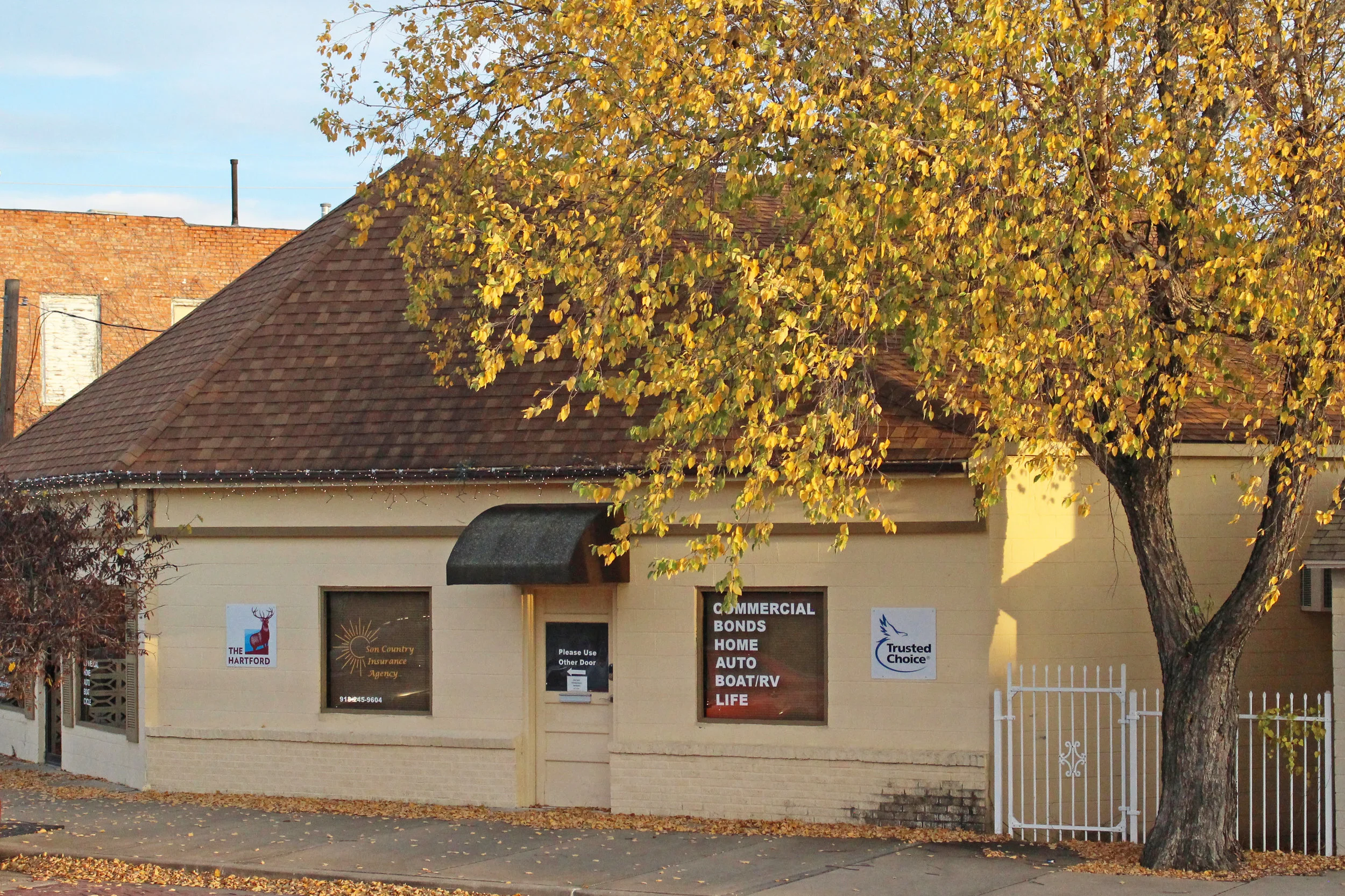 A large yellow autumnal tree frames in a white stucco Son Country Insurance building in downtown Sand Springs, Oklahoma