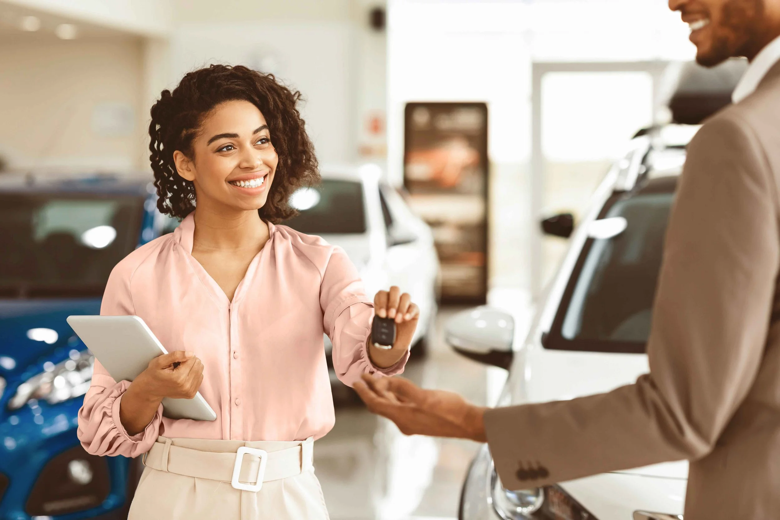 Black car sale woman handling car key to new auto owner.