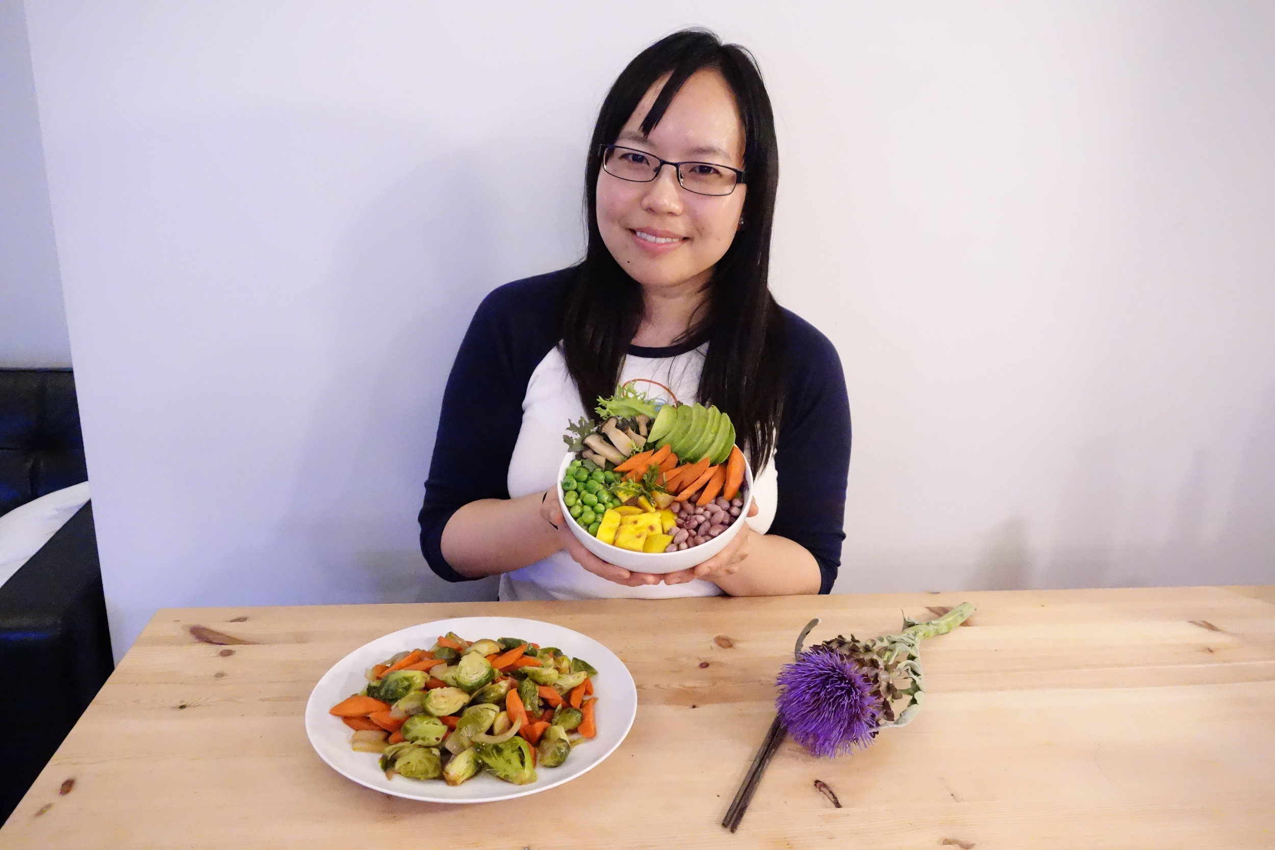 Sandy Leung from SandyByTheBay.com food blog, holding the Vitality Bowl. Maple Glazed Brussels Sprouts (On The Table). Recipes from MeatLess .