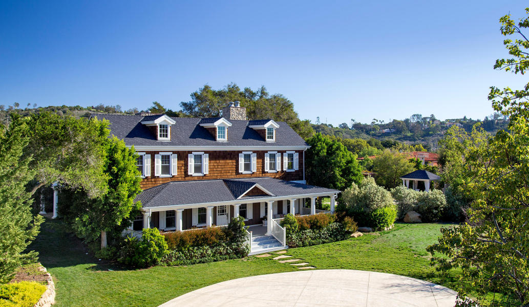 A New England-style home sits behind a tree-lined drive and gates on Featherhill Road in Montecito