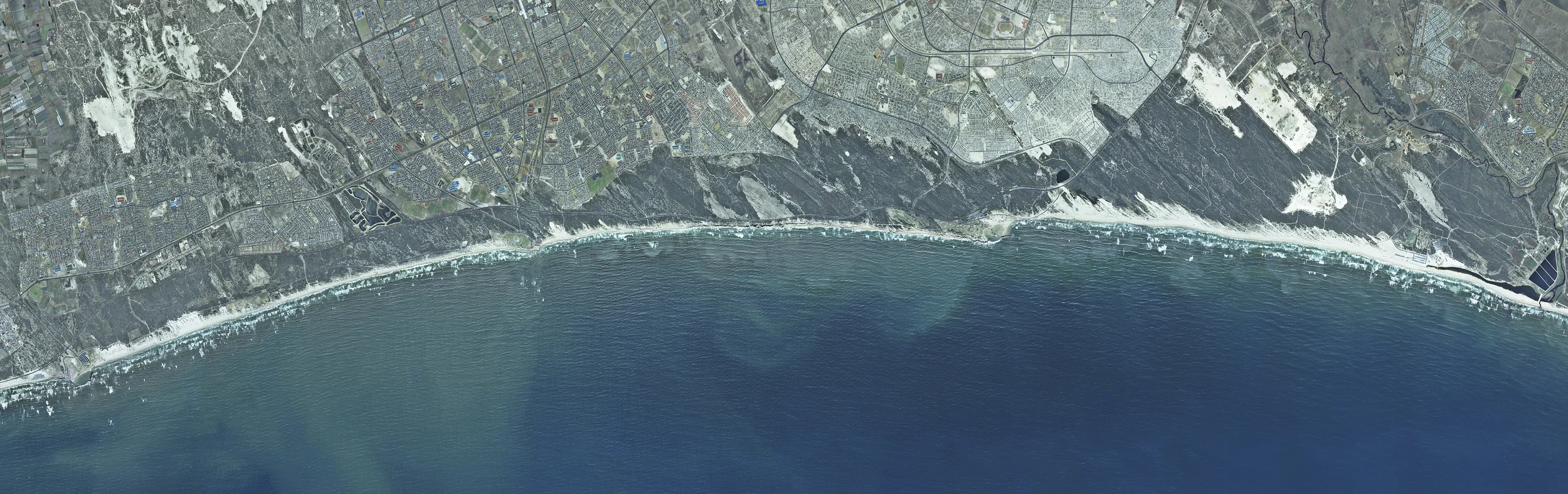 False Bay #1 This aerial view depicts the former separate amenities of Strandfontein Pavilion, Mnandi Resort, Monwabisi Resort and Macassar Resort. This stretch of coast, notorious for dangerous swimming conditions, was divided into sections for ‘black’ and ‘coloured’ recreation during apartheid. 2011 Archival Pigment Ink on Cotton Paper 31.5 x 92.5 inches