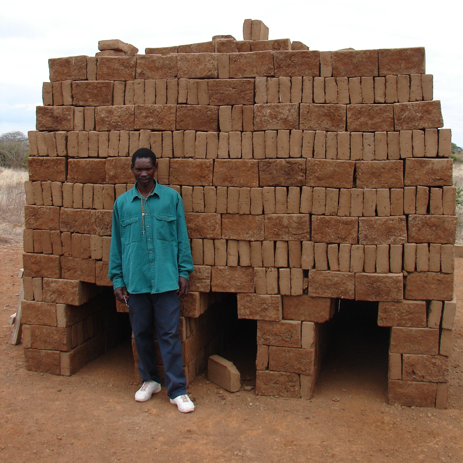 A mason stands in front of a pile of clay bricks - Tanzania
