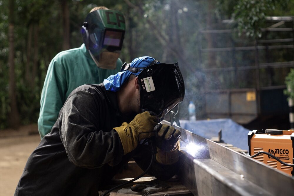 Volunteer Rickey (front) begins welding while architecture student Marco (rear) watches