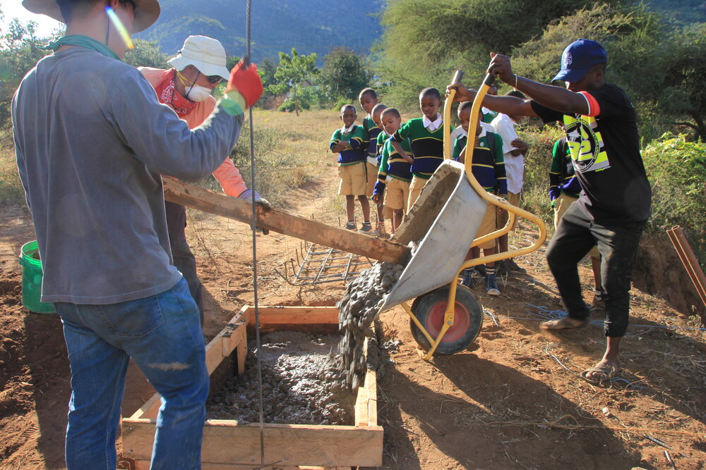 Cal Poly volunteers work with the Mbesese build team to pour concrete for the new foundations