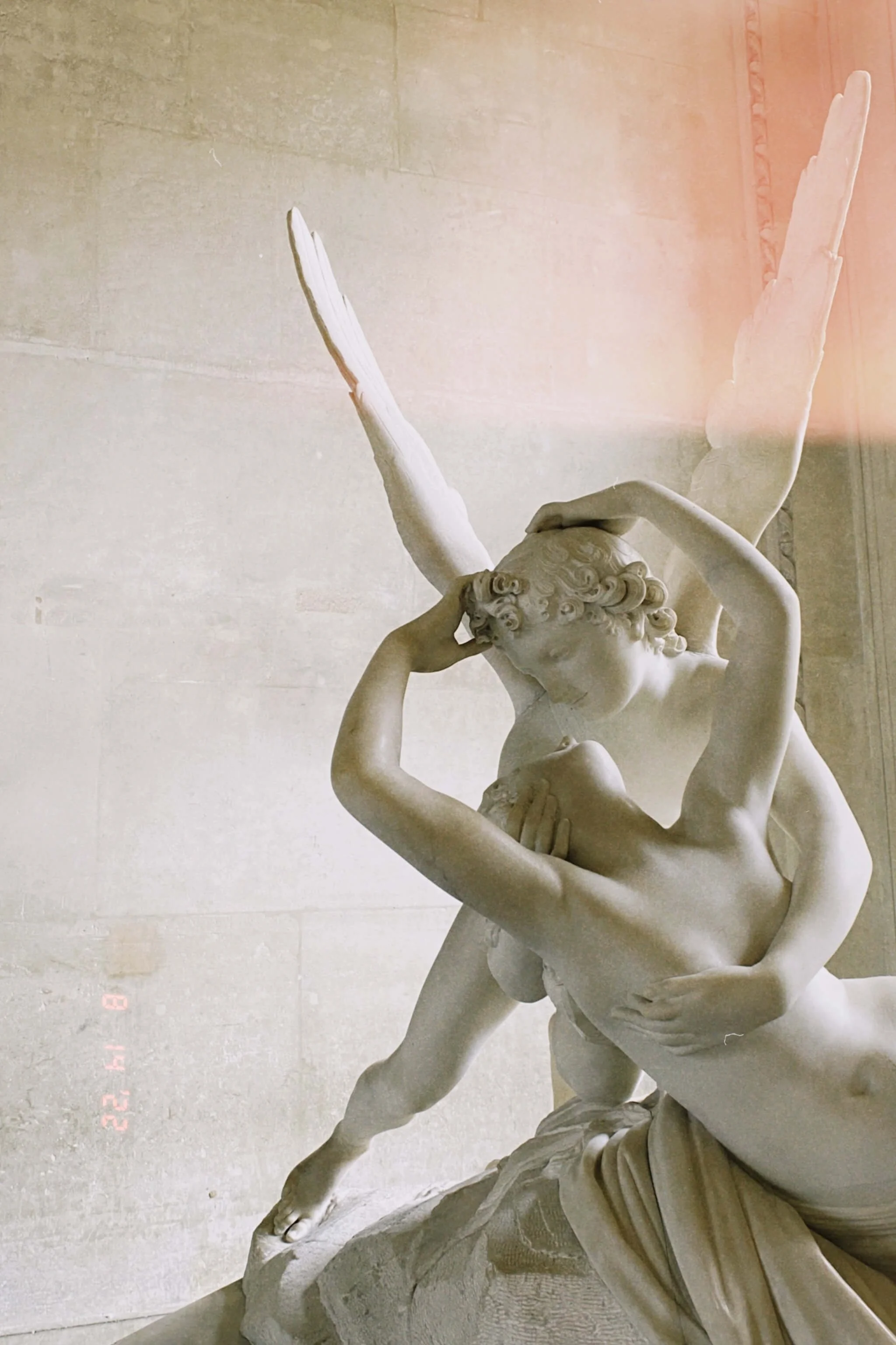 A classical marble sculpture of two figures, one male and one female, engaged in an intimate pose. The male figure appears to be holding and supporting the female figure, who is leaning into him with her face close to his. The sculpture is detailed with flowing hair and realistic anatomy, and is set against a plain background.