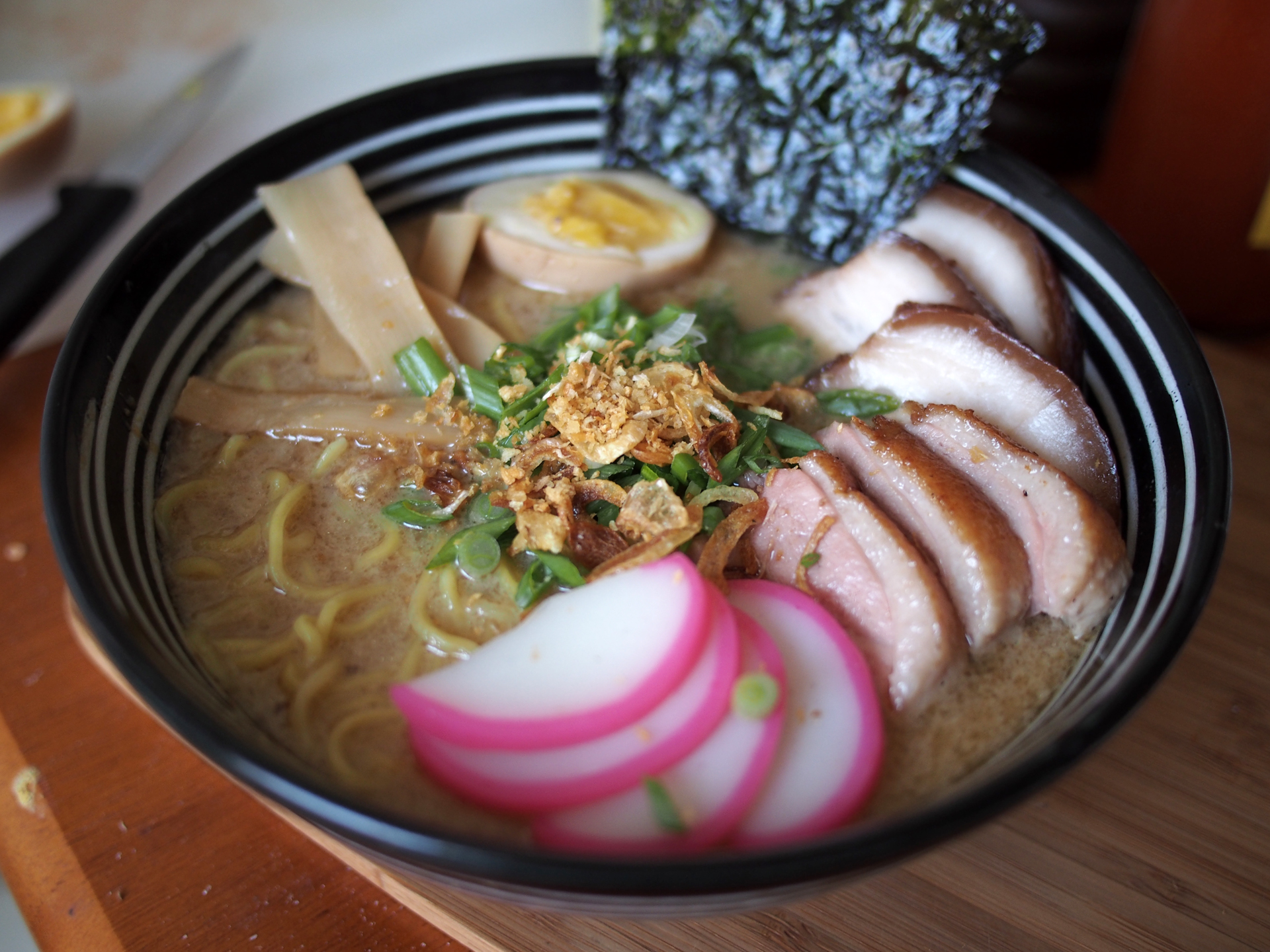 Tonkotsu/Duck ramen with sous vide pork belly chashu, sous vide duck breast, fish cake, and seasoned medium-boiled egg topped with menma, green onion, fried shallot, fried garlic, and nori strips.