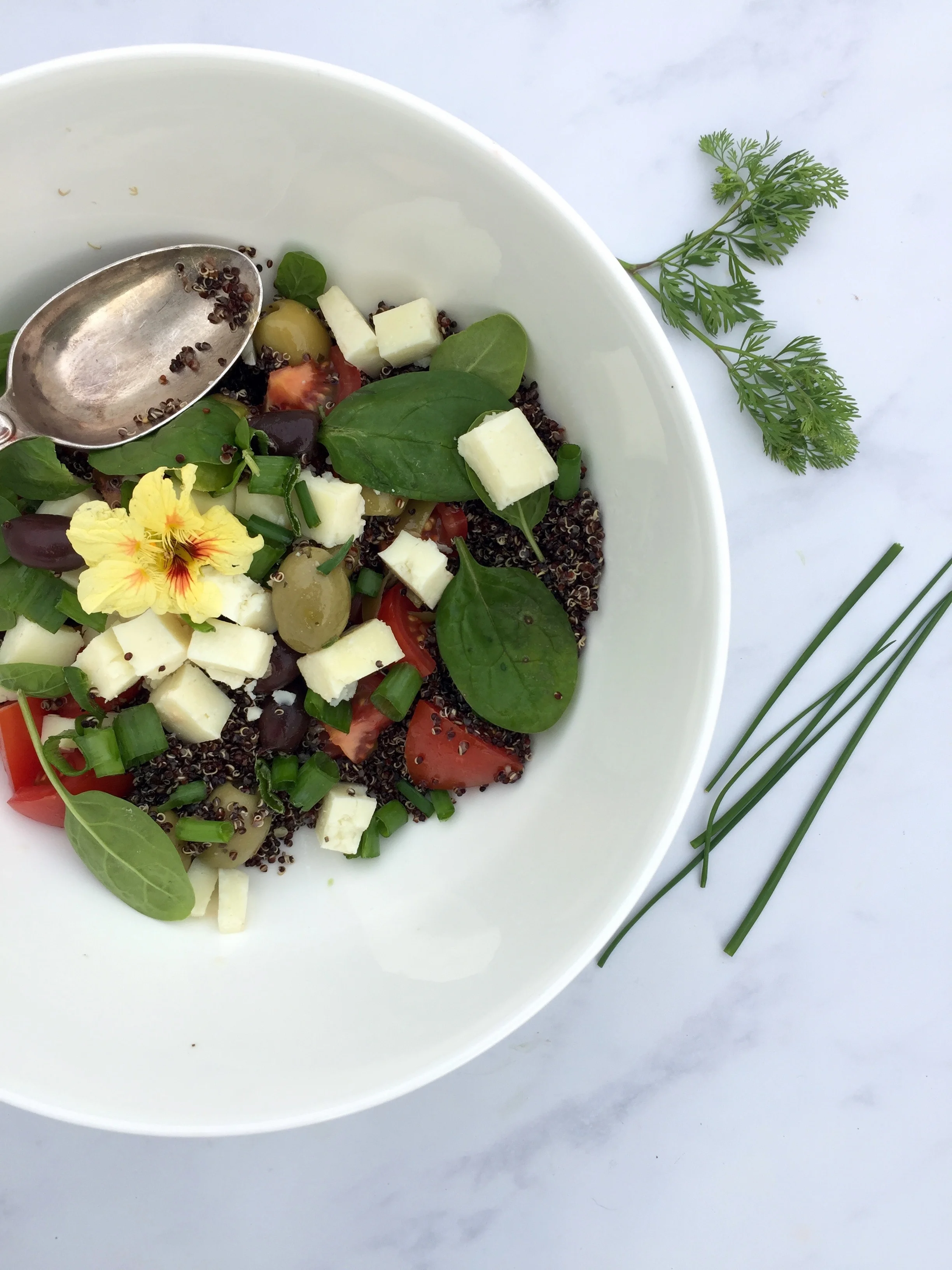 Quinoa salad with feta, olives, tomatoes spinach & a nasturtium. 