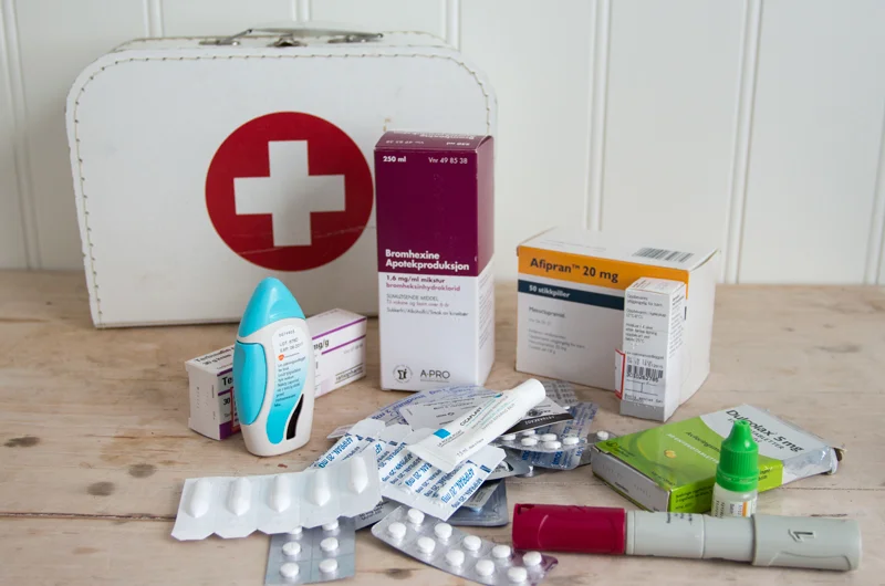 Førstehjelps-kofferten i bakgrunn. ALT foran er gamle medisiner som har gått ut på dato og som skal leveres til apoteket.