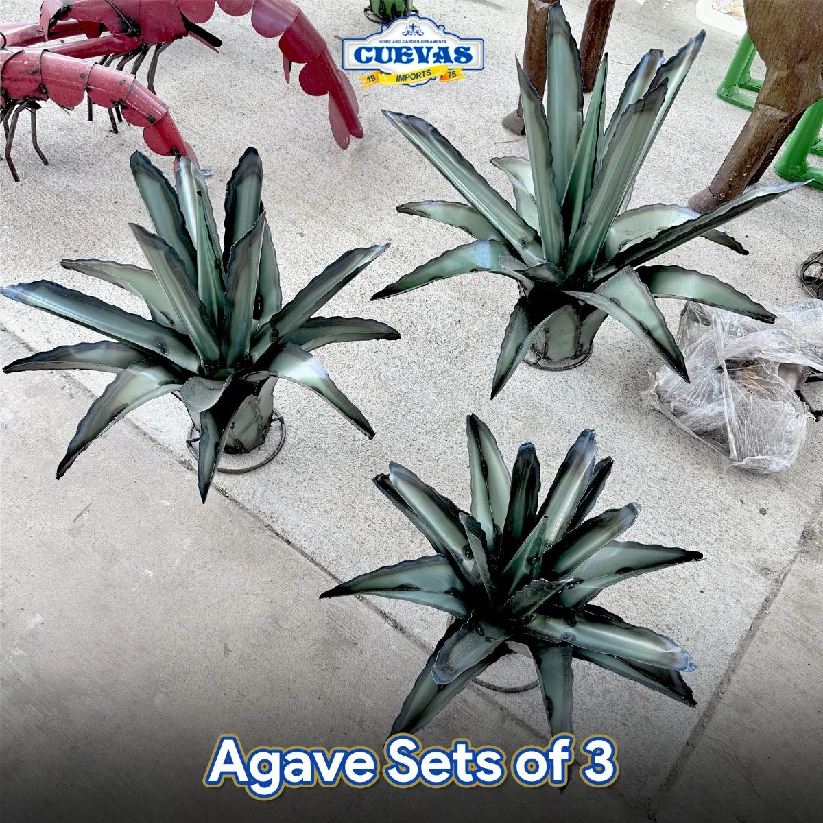 Set of three metal agave-shaped plant sculptures with pointed leaves, painted in shades of green, black, and silver, displayed on a concrete floor.