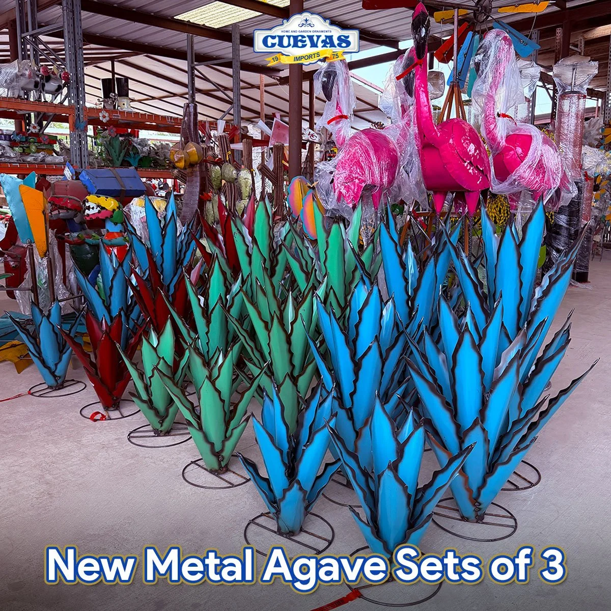 Colorful metal agave garden ornaments resembling large cacti in blue, green, and red with black accents, displayed in an outdoor store with shelves of other garden decor.