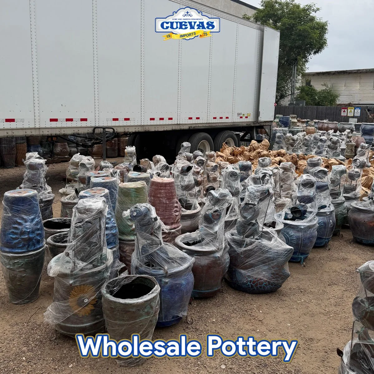 Outdoor scene with numerous colorful pottery vases wrapped in plastic and stacked on dirt ground, with a large white truck in the background. Text overlay reads "Wholesale Pottery".