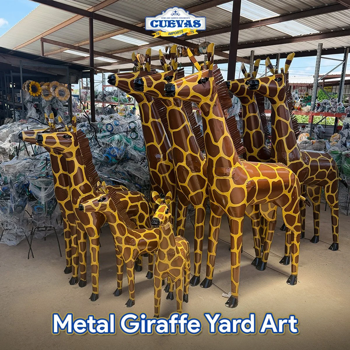 Metal giraffe yard art display featuring several large and small metal giraffe sculptures with a yellow and brown color pattern, set against a background of other yard ornaments and decorations in a covered outdoor marketplace.