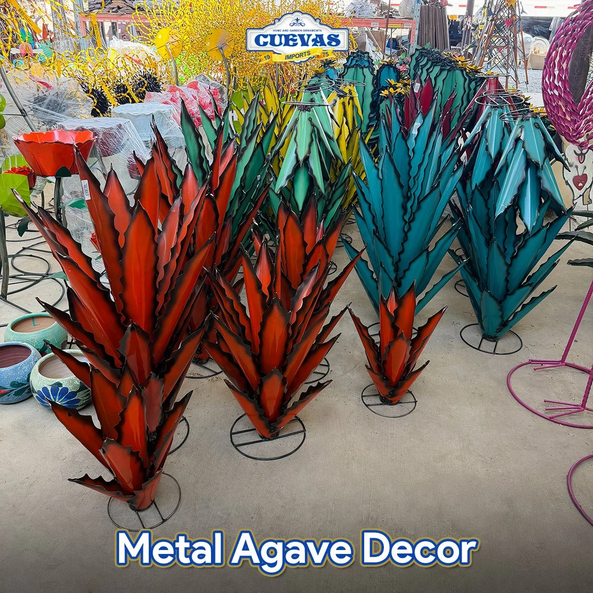 Colorful metal agave-shaped garden and home decor ornaments in red, blue, green, and teal, displayed upright on black metal stands at a store.