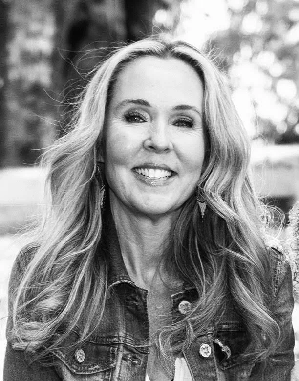 A smiling woman with long wavy hair wearing a denim jacket outdoors, black and white photography.