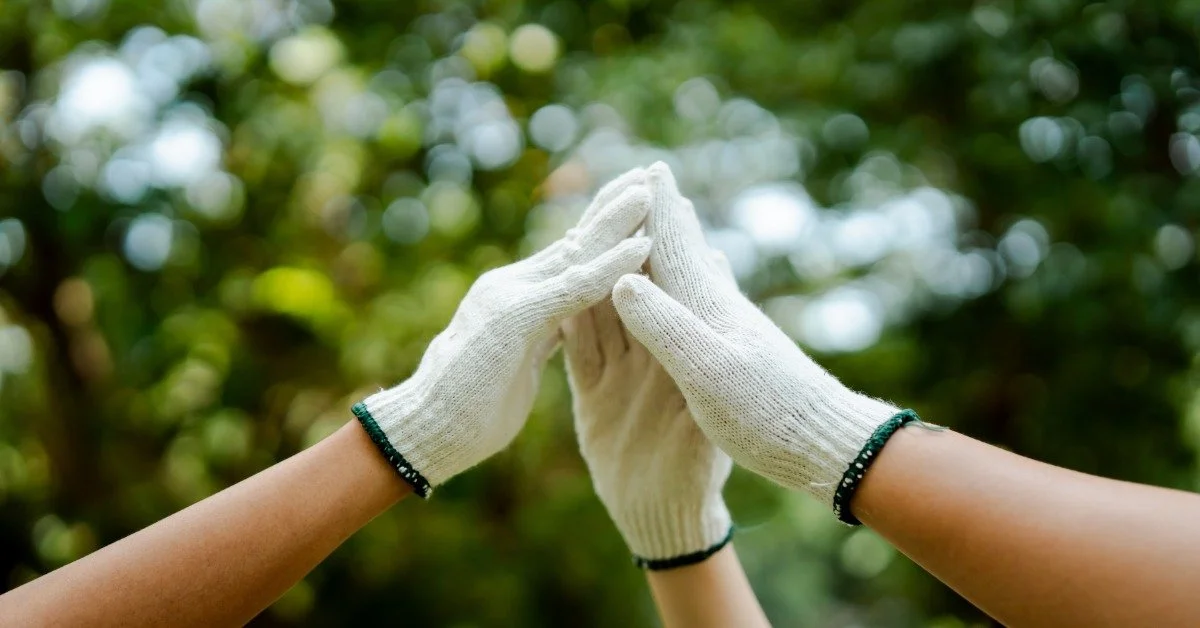 Three people wearing white gloves outside. All three people outstretch their hands in a supportive motion.