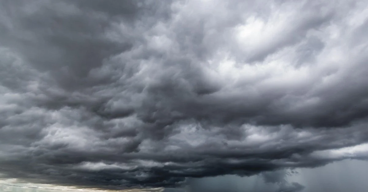 Many dark gray clouds cover the sky as a storm forms above the ground. Minimal sunlight is visible in the distance.