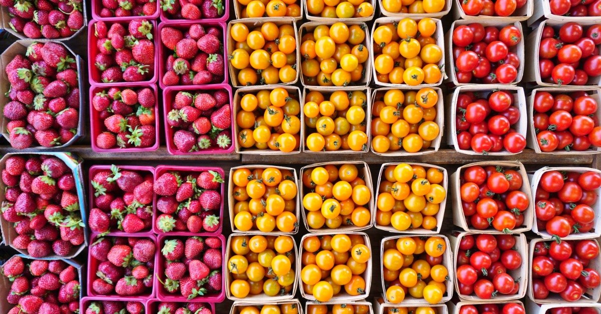 Many baskets full of colorful strawberries and tomatoes. Most of the tomatoes are yellow, the rest are red.