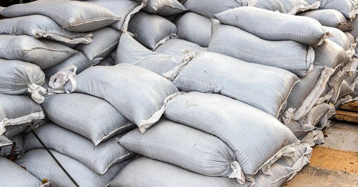 A massive pile of long white sandbags sitting on a wooden platform outside. The platform is made of long wooden planks.