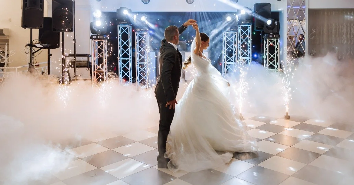 A bride and groom dancing on a checkered dance floor surrounded by atmospheric smoke from a fog machine.