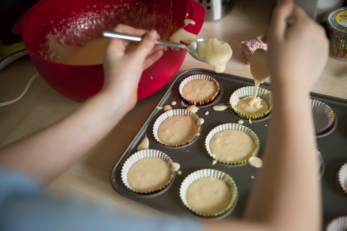 Image of girl putting cake mixture into colour cup cake cases. 