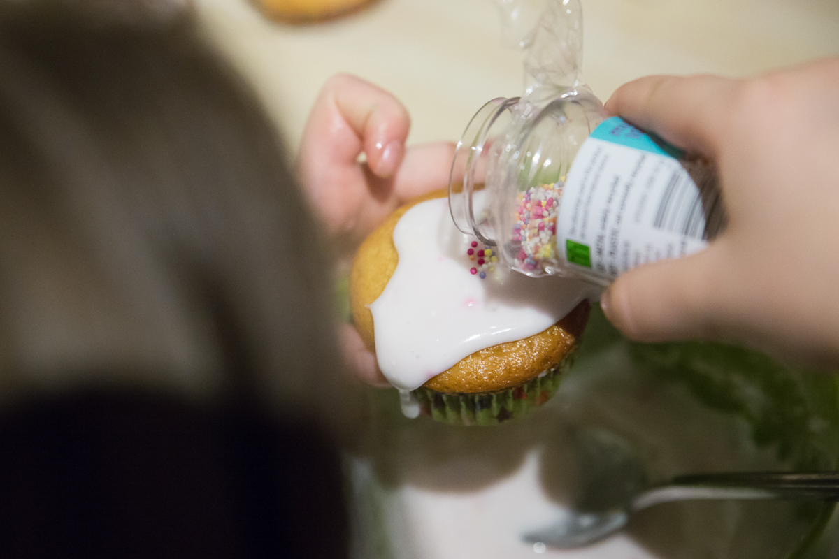 Little girl adds sprinkles to an iced cupcake.