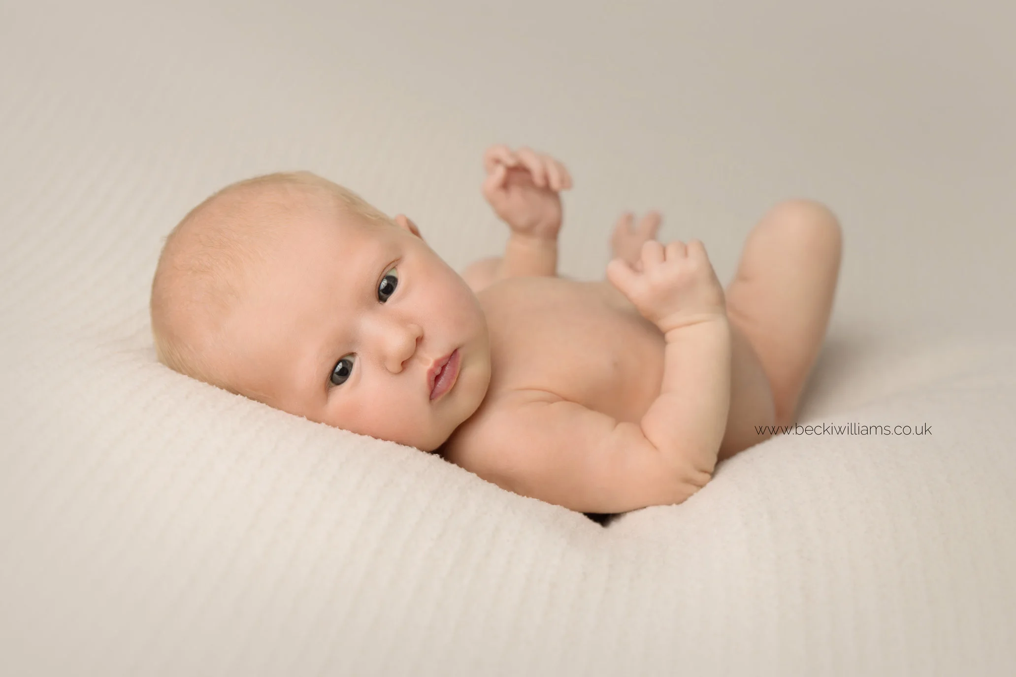 newborn baby laying awake on a cream blanket during her newborn photo shoot in hemel hempstead