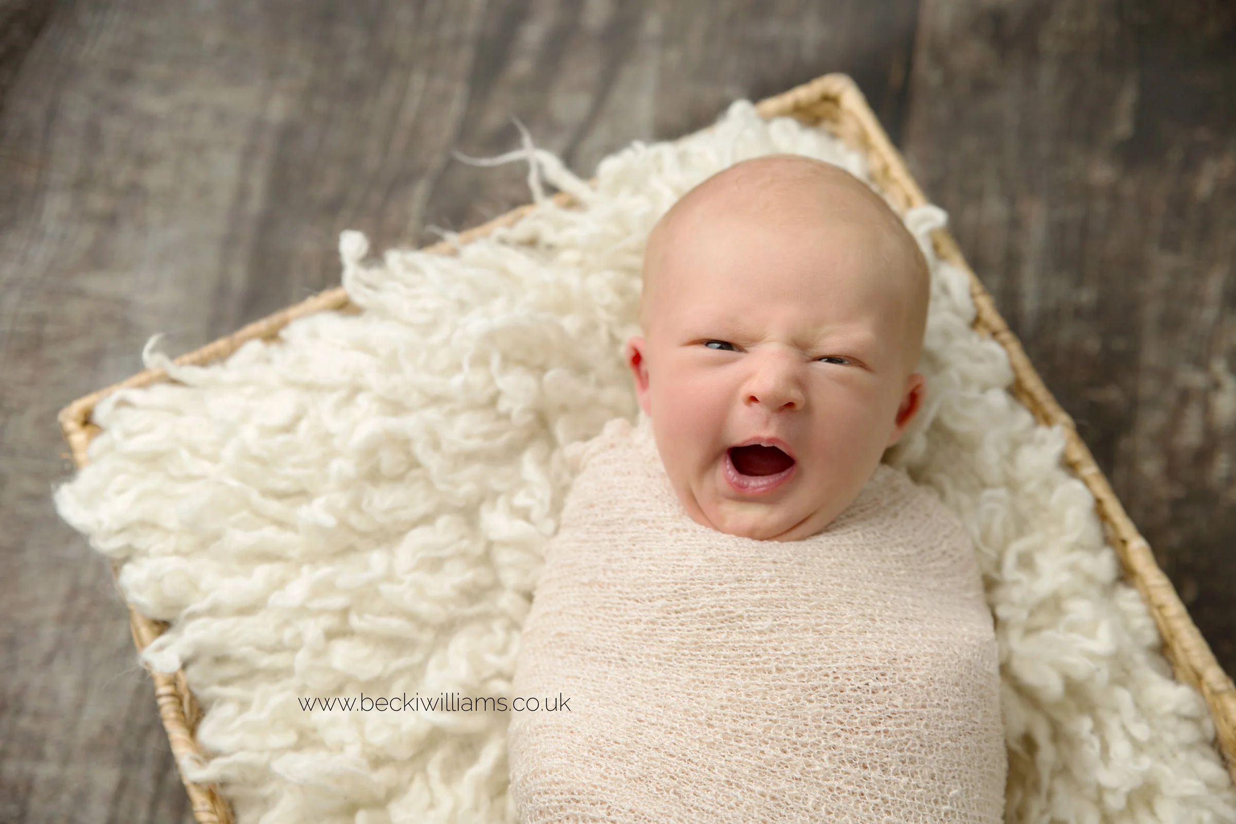 newborn baby girl laying on a basket, yawning at her newborn baby photo shoot in hemel hempstead