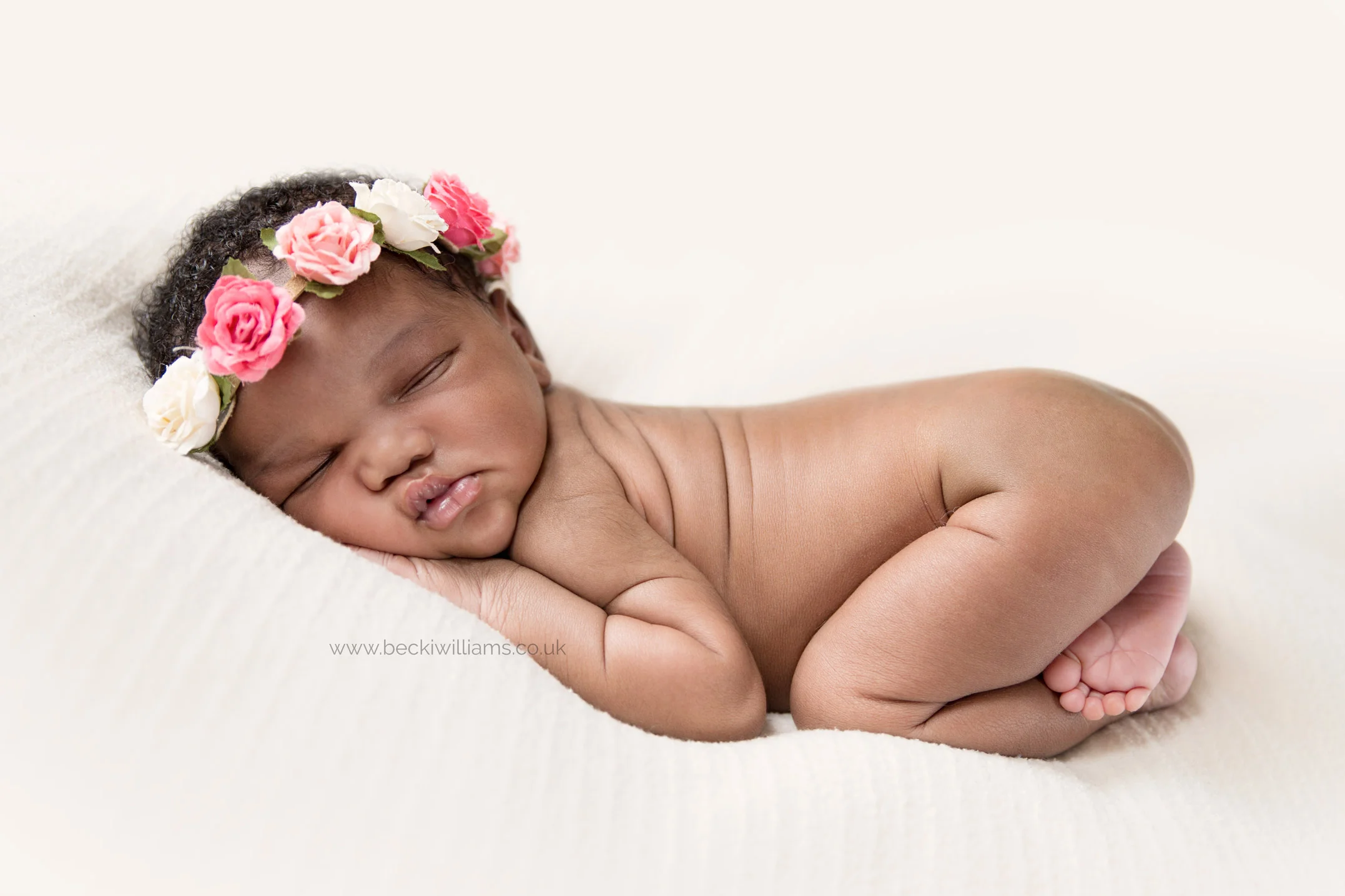 newborn baby girl laying on her tummy wearing a flower brown at her newborn photo shoot in hemel hempstead