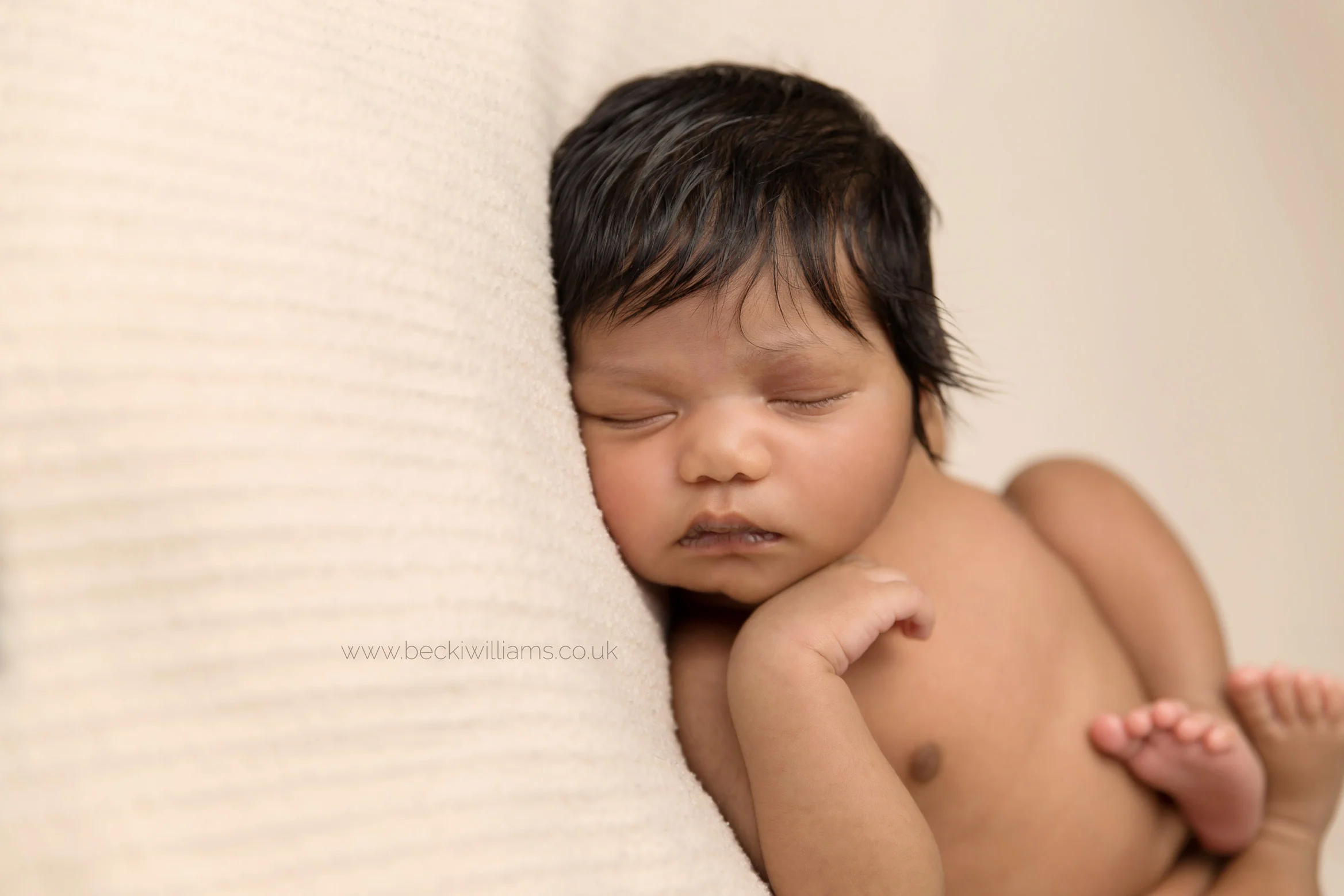 newborn baby girl laying on her back on a cream blanket for her newborn photo shoot in hemel hempstead