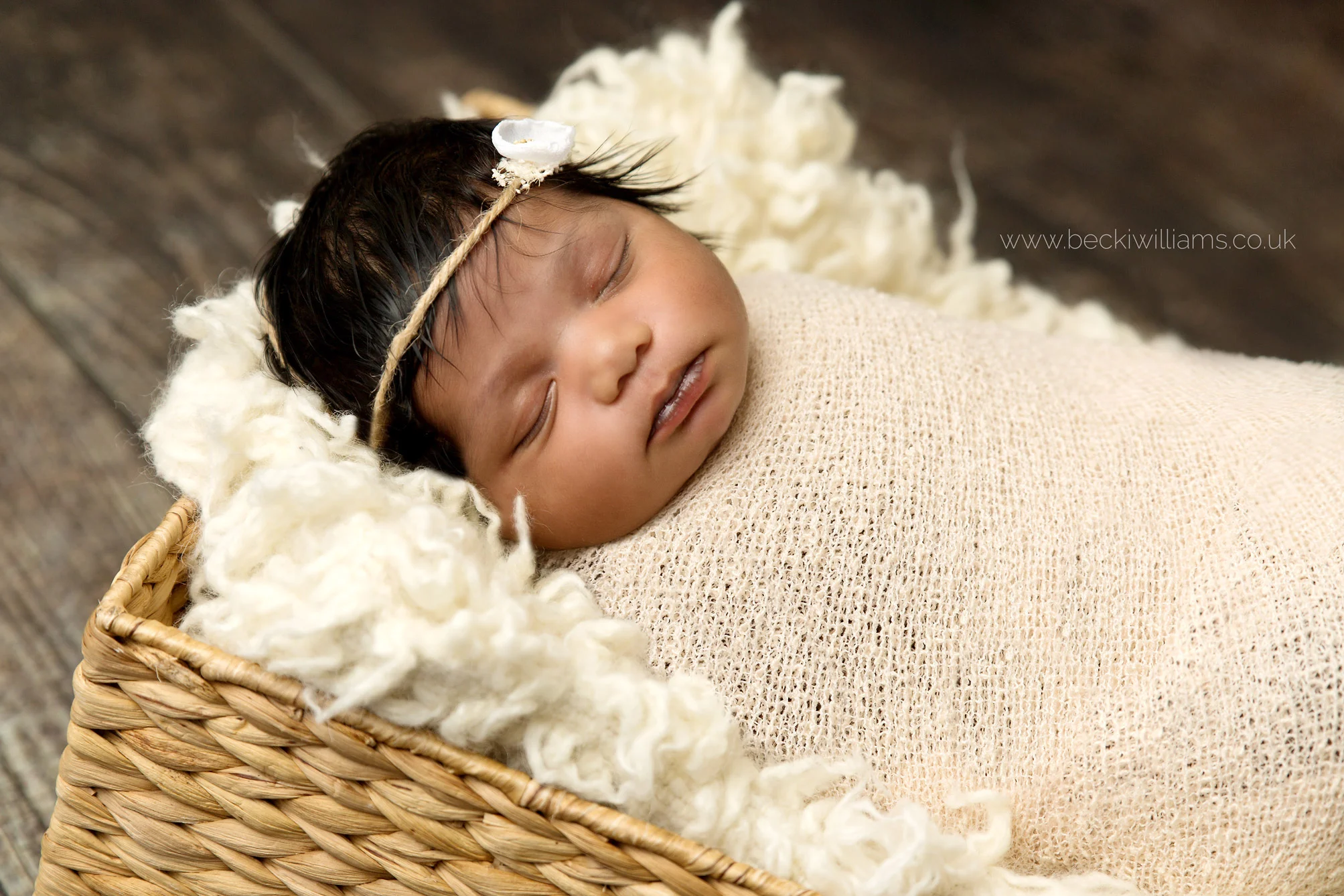 newborn baby girl wrapped in a cream wrap in a basket on a wooden floor